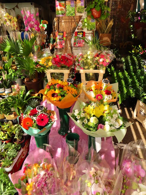 A display of fresh floral bouquets arranged in various colorful compositions, featuring vibrant roses, gerbera daisies, and mixed pastel flowers wrapped in decorative paper and cellophane. The bouquet