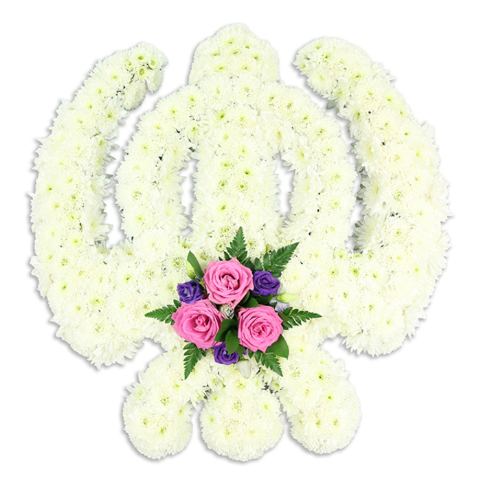 In this image, a stately Sikh Khanda funeral tribute appears to float in front of a pure white background, its sacred outline shaped entirely by white chrysanthemum blossoms. The core of the design is the upright double-edged sword, strong and centred, held within the smooth circle of the chakkar. Flanking it, the two kirpans sweep gracefully outward and downward, their forms made clear by the careful, almost sculptural placement of each bloom. The chrysanthemums are small and tightly packed, with intricate petals that fold inwards like tiny cushions; together they create a thick, uniform texture that feels soft yet substantial, as though the symbol is wrapped in a gentle, protective layer. The white and pale cream tones merge into a tranquil, almost luminous surface. At the base, where the blades of the kirpans meet, a contrasting accent posy introduces gentle colour and emotion. Three fresh pink roses sit at the heart of this cluster, their petals unfurling in spirals of blush and rose-toned cream. Around them, deep purple flowers provide a solemn counterpoint, while light, feathery ferns and rich green foliage add airiness and structure. A subtle drop shadow beneath the tribute hints at depth, suggesting the care taken in both the design and presentation. This floral Khanda would be especially meaningful for Sikh families in Shepperton planning funeral or memorial flowers, perhaps delivered by Flowers Shepperton to quiet streets near the High Street, to riverside homes along the Thames, or to nearby community spaces. It serves as a tender, respectful way to reflect spiritual devotion, family love, and the enduring bonds of heritage at a time of farewell.