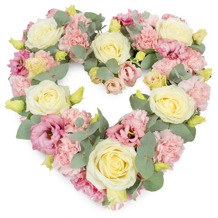A full, symmetrical heart-shaped wreath of pastel flowers appears against a bright white backdrop, its form and colours carefully balanced, as if lovingly prepared for a Shepperton family wanting to say a gentle goodbye. The heart is densely filled from edge to edge, giving it a lush, complete appearance without any empty spaces, like a visual metaphor for a life rich in connections. Large cream and pale yellow roses act as anchor points throughout the design, their velvety petals spiralling outward and catching the light, evoking warmth, gratitude, and enduring devotion. Between these roses, soft clusters of light pink carnations fill the gaps, their many fine, frilled petals creating a soft, almost feathery texture that smooths the outline of the heart. Deeper pink and mauve lisianthus blooms are scattered gracefully among them, with slightly more open, layered petals that add variation in shape and hue, suggesting the complexity and depth of shared memories. Silvery-green eucalyptus, with its rounded, matte leaves, winds delicately through the flowers, adding cool tones and subtle structure, much like the quiet, leafy lanes and towpaths that characterise Shepperton. Small yellow-green buds are tucked throughout the arrangement, tiny points of freshness that hint at new beginnings and the continuity of love beyond loss. The overall mood is tranquil, comforting, and respectful, suitable for resting on an easel during a service at a local chapel or placed beside a casket at a crematorium. This heart-shaped tribute speaks of closeness, compassion, and the way a community like Shepperton gathers around families in their time of grief.